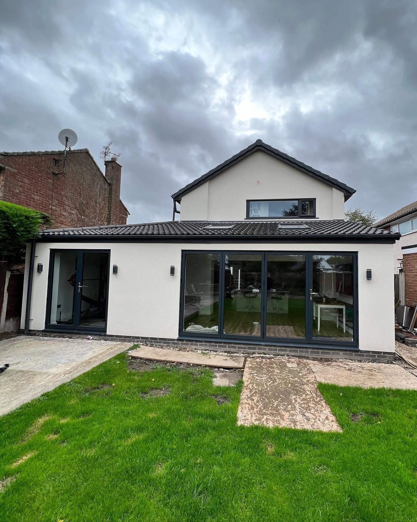 Completed single-storey rear house extension with bifold doors and white render, Greater Manchester